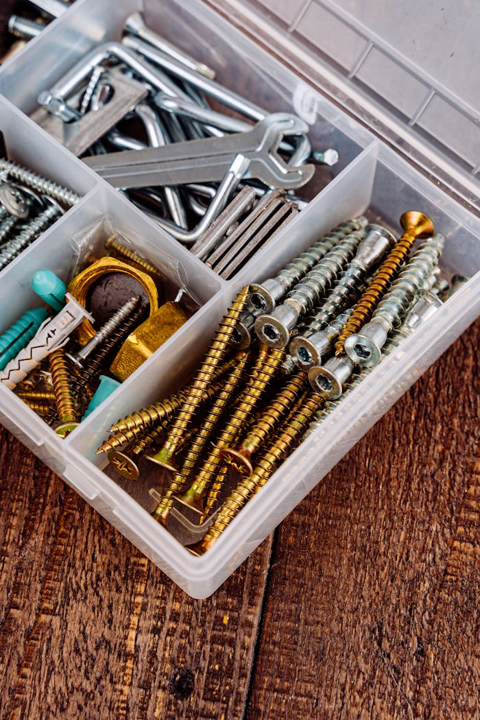 Close-up view of a toolbox containing assorted screws, wrenches, and tools on a wooden surface.